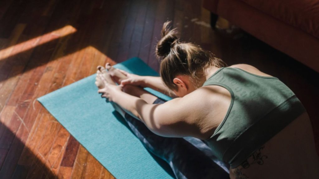A woman engages in integrative yoga on a mat, basking in sunlight, promoting relaxation and inner peace.
