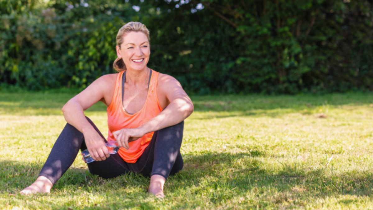 A woman relaxes on the grass, looking happy and healthy, surrounded by a peaceful natural environment.