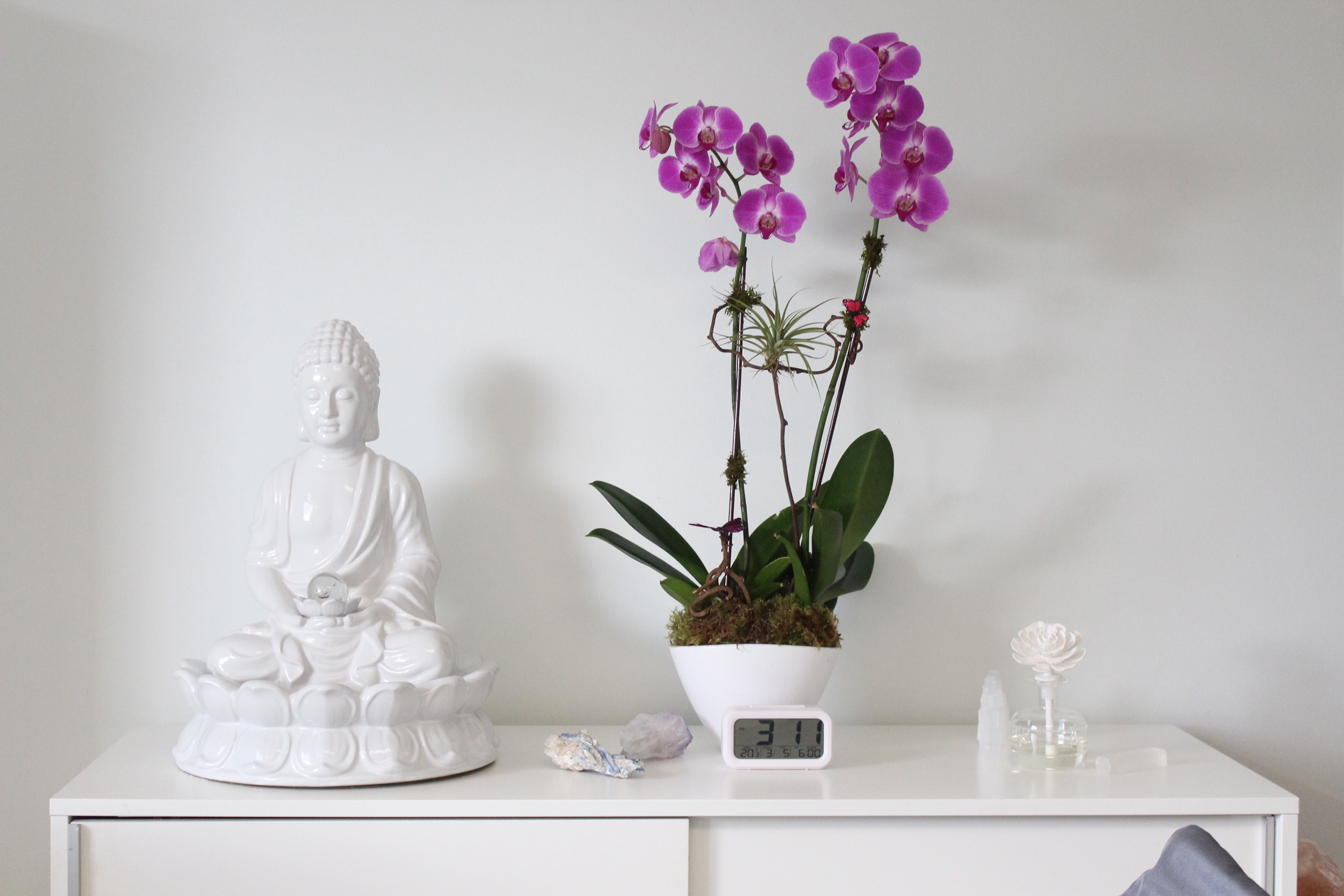 A white dresser featuring a serene Buddha statue beside a vibrant purple orchid in a decorative pot.