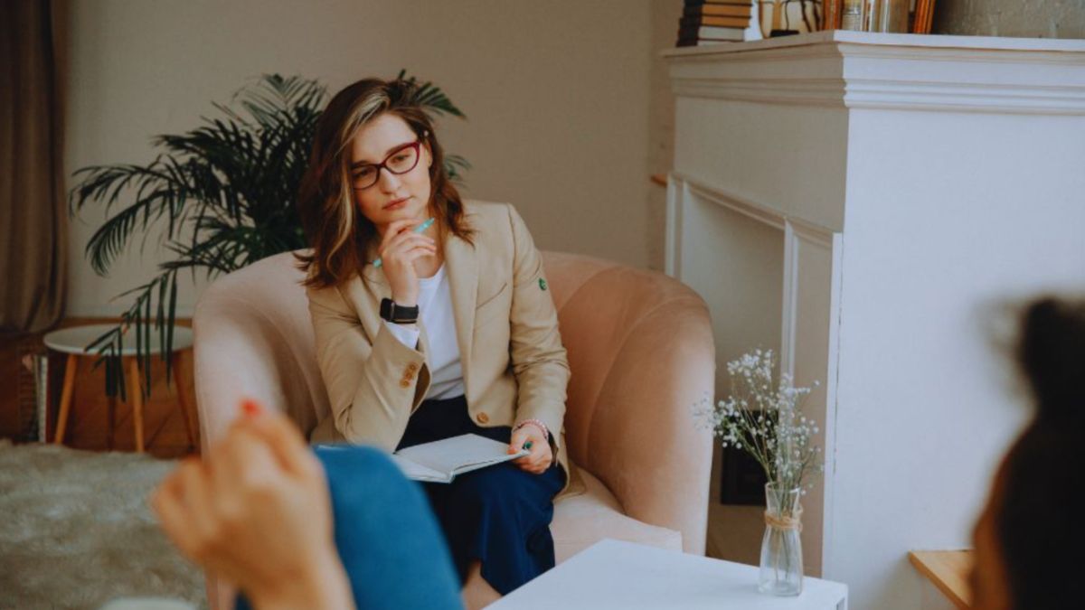 A career transition coaching session with a professional coach attentively listening to a client in a cozy, well-lit room with a notebook in hand, creating a supportive environment for personal and career development.