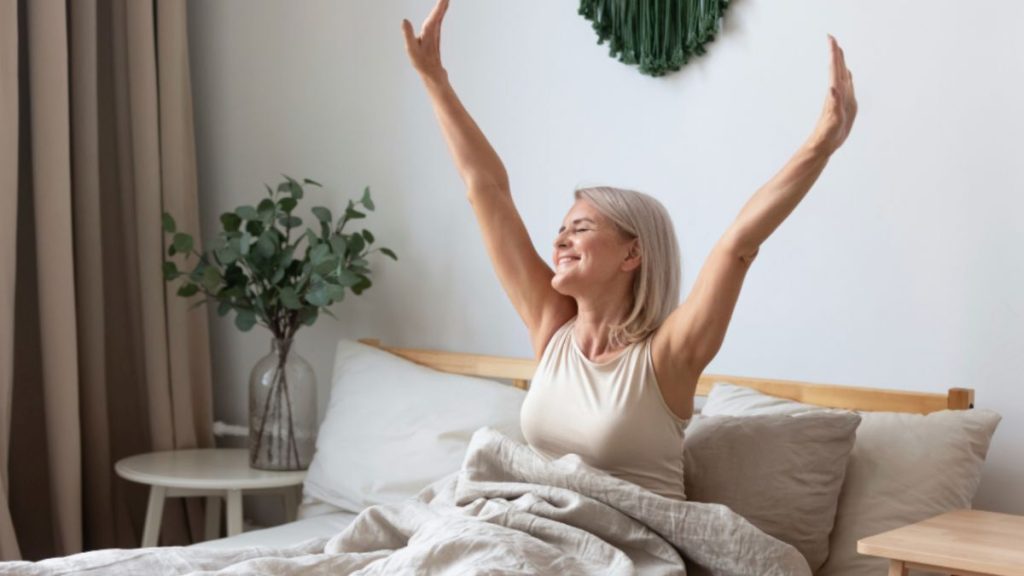 A joyful woman sitting on her bed with arms raised—expressing the relief and confidence achieved after life coaching in Miami.