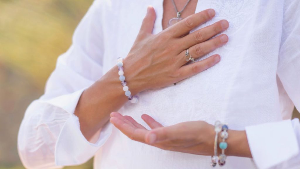 A woman holds her hands together, featuring a chakra bracelet, reflecting her dedication to spiritual life coaching.