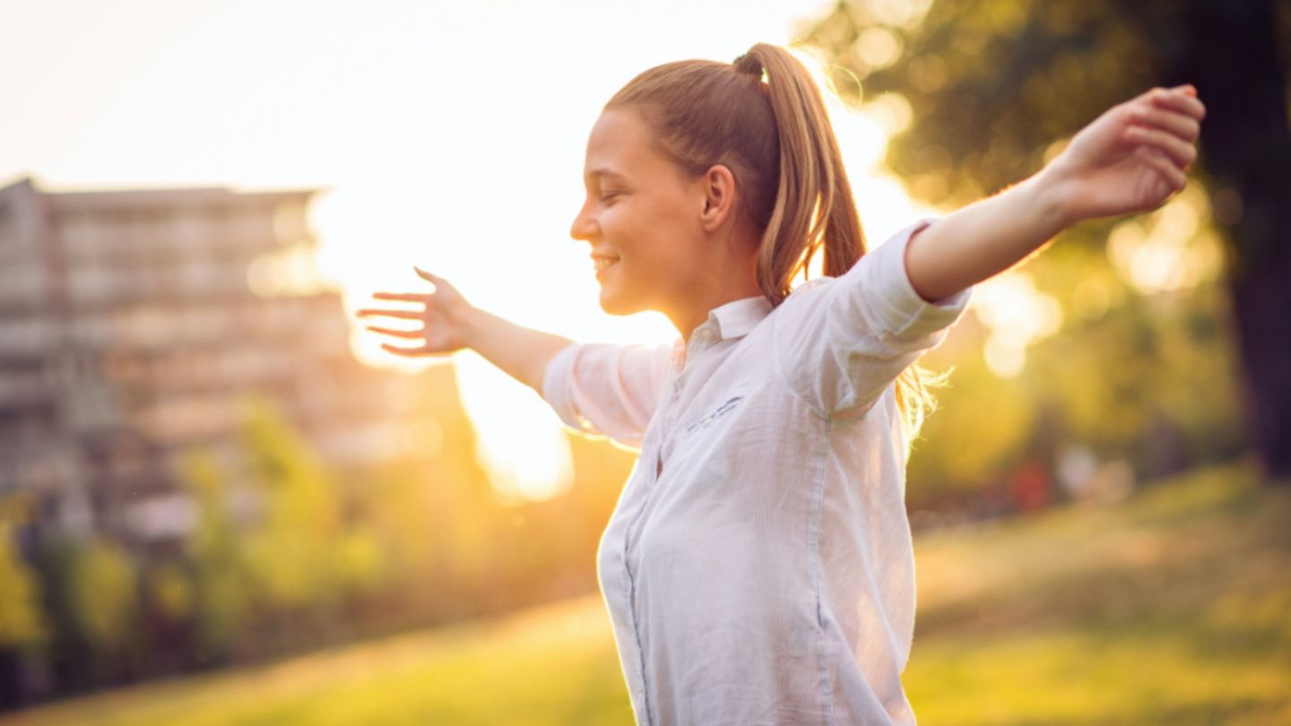 A woman stands in a field with arms outstretched, embodying chakra energy and spiritual life coaching principles.