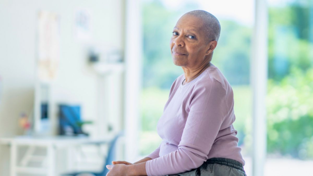 An older cancer patient sits on a chair, showing the positive effects of the support she got from a lymph drainage therapist.