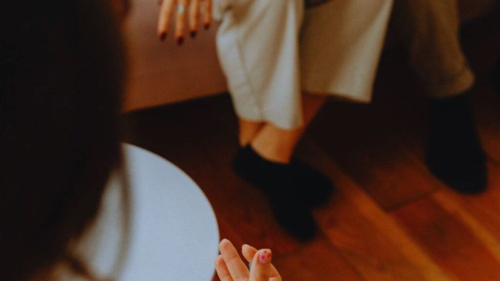 A life coaching session focused on personal growth, showing one person listening with attention while the other gestures calmly, capturing a moment of engaged, supportive communication and growing self-awareness.