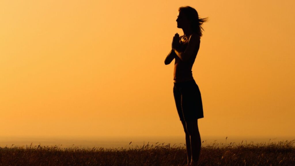 Woman's silhouette standing in grass at sunset, representing empowerment in spiritual life coaching.