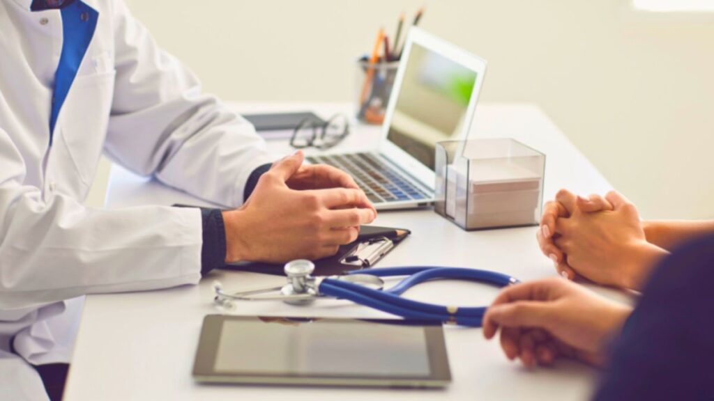 An oncologist discusses lymphedema therapy with two patients at a desk, providing education and support.