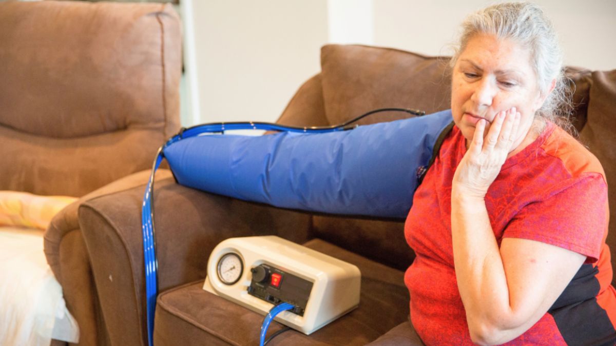 A woman sitting on a couch with a compression sleeve fitted on arm for post-surgical care.