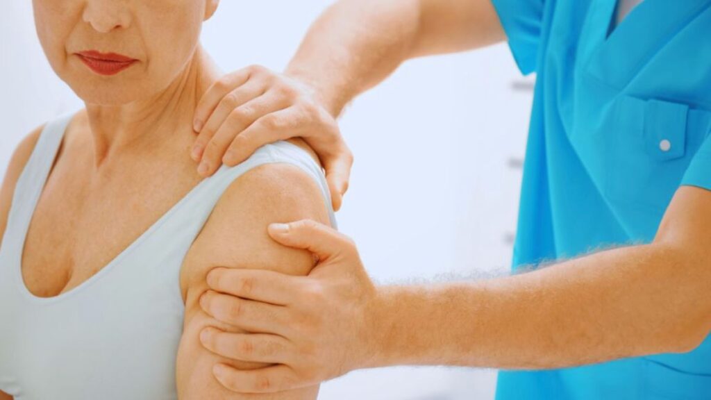 A manual lymphatic drainage therapist in South Miami, FL, wearing medical scrubs, gently positions and supports the arm and shoulder of an older woman during a therapeutic session focused on reducing swelling.