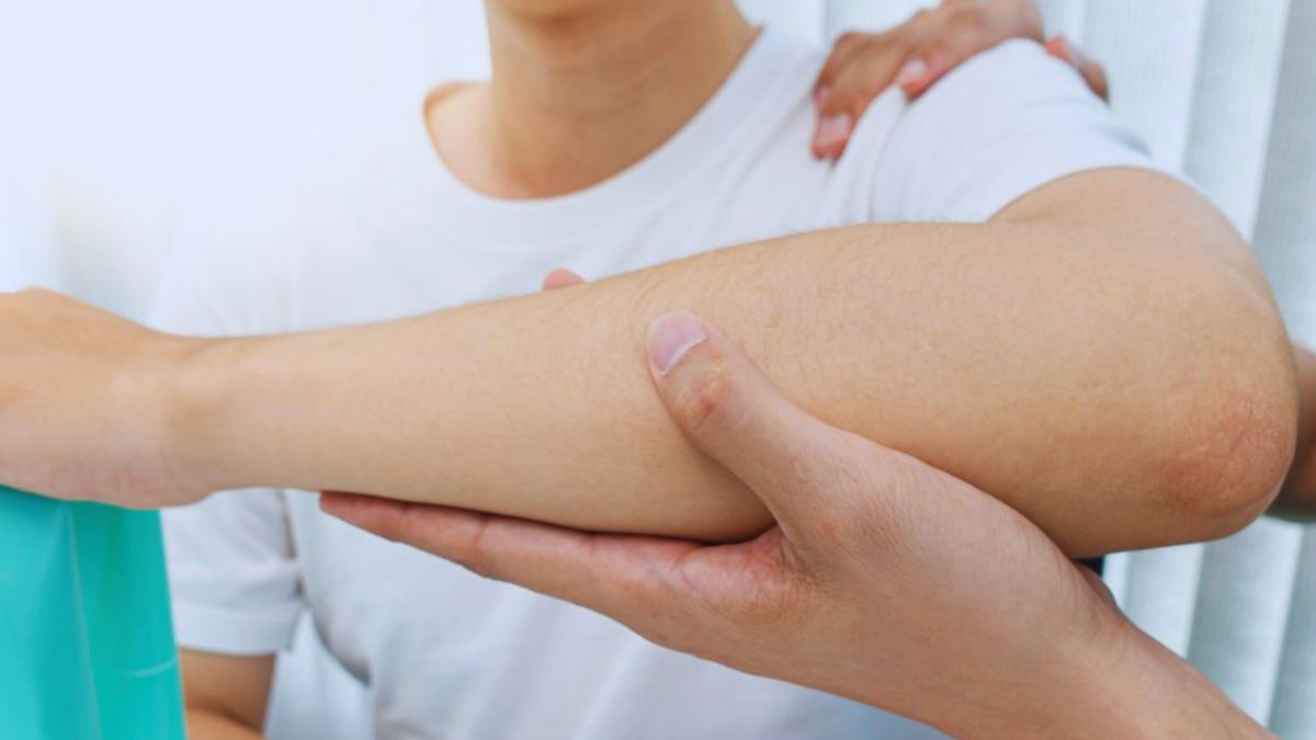 A manual lymphatic drainage therapist holds and gently supports a person's bent arm at the elbow during a therapy session, focusing on reducing swelling.